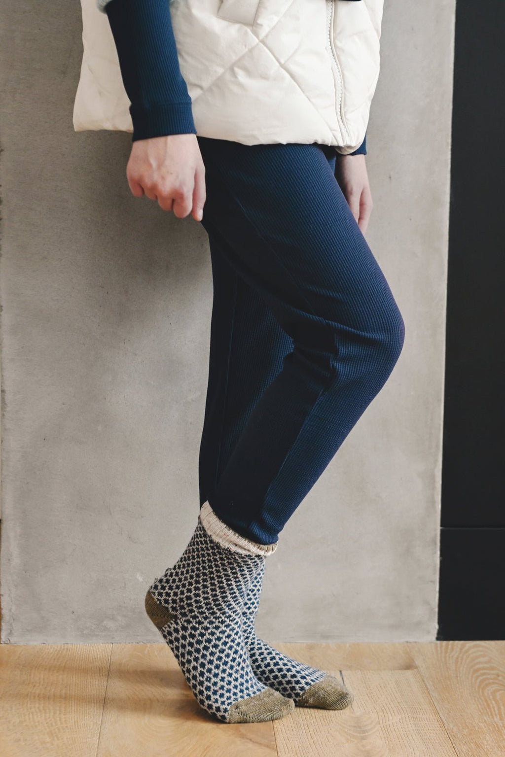 A person wears Cozy Earth Children's Bamboo Waffle Knit Base Layer Pant while standing on a wooden floor in front of a gray wall.|Color:Navy