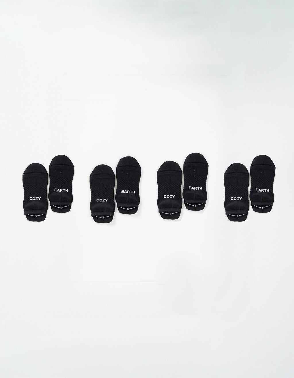 Four pairs of black Essential Ankle Socks by Cozy Earth are arranged in a row on a white background, each pair featuring "COZY" and "EARTH" in white text on the toes. |Color:Black