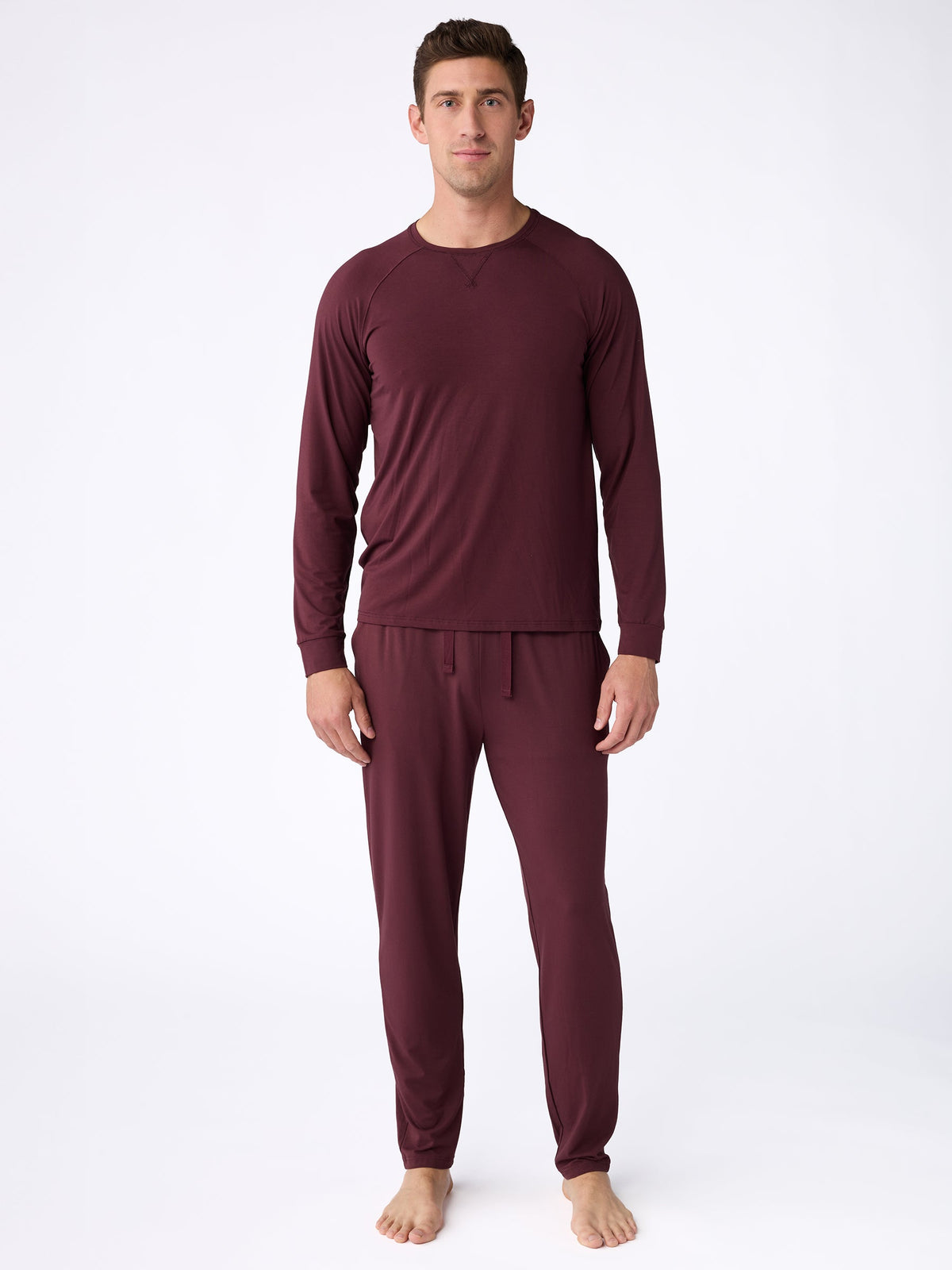 A man stands barefoot on a plain white background wearing a matching maroon Men's Ultra-Soft Bamboo Pullover Crew by Cozy Earth. He is facing forward with a neutral expression. |Color:Burgundy