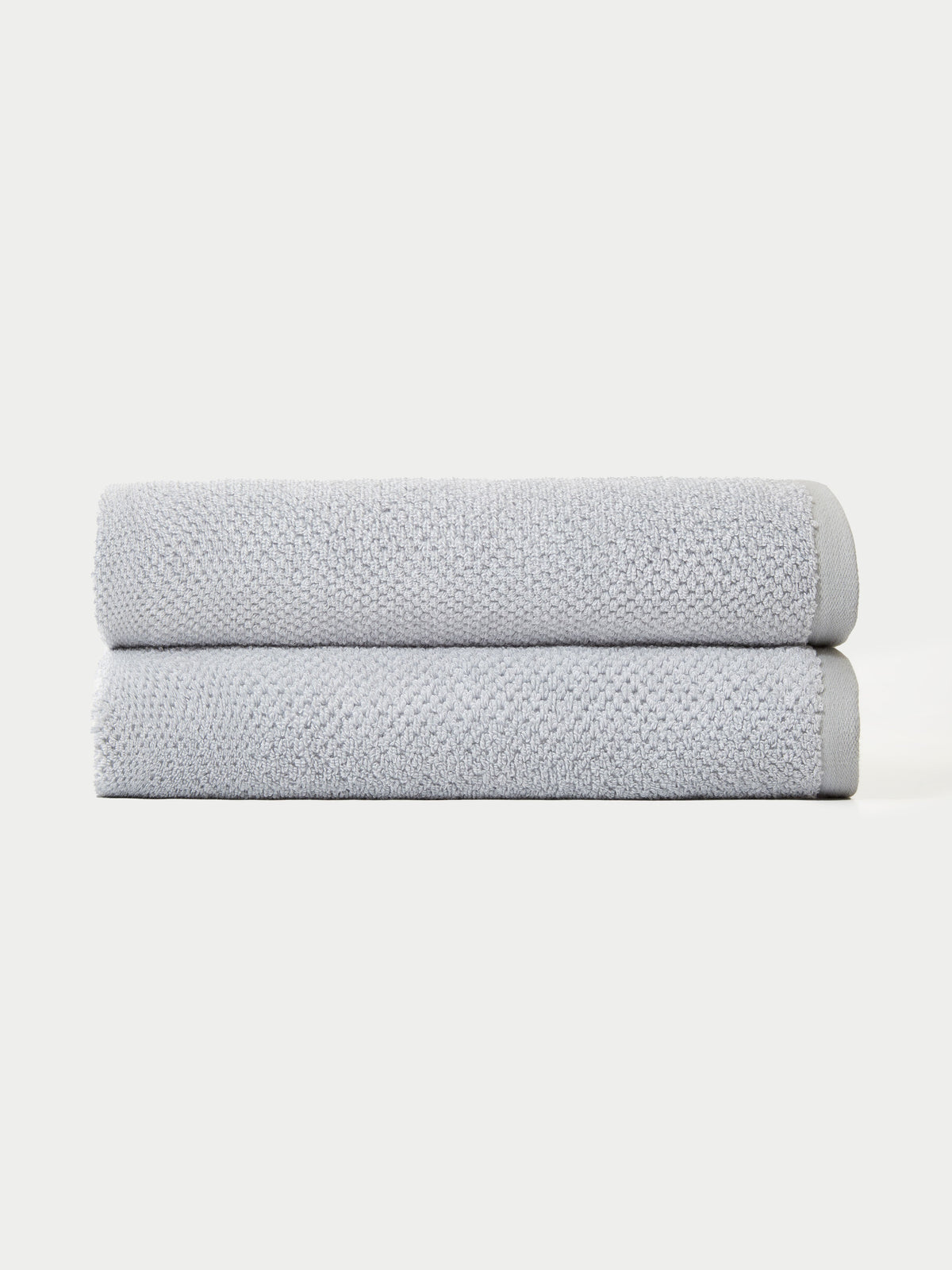 The Nantucket Bath Towel Set by Cozy Earth features two neatly folded light gray towels stacked together against a plain white background.|Color: Heathered Harbor Mist
