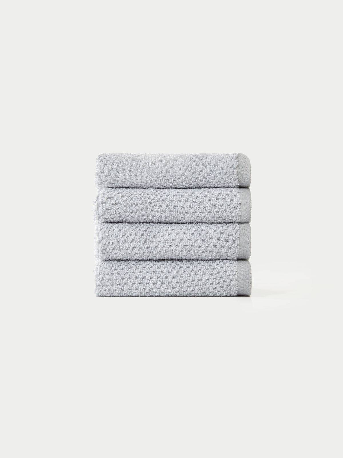 A neatly stacked pile of four light gray, textured towels from the Cozy Earth Nantucket Bath Towel Set on a plain white background.|Color: Heathered Harbor Mist