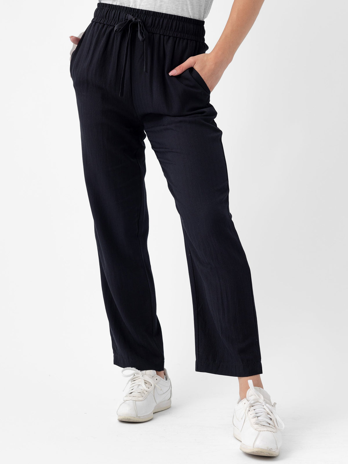 Person wearing Cozy Earth's Women's Sunset Cropped Pant in Jet Black with hands in pockets and white sneakers. The background is plain white. |Color:Jet Black