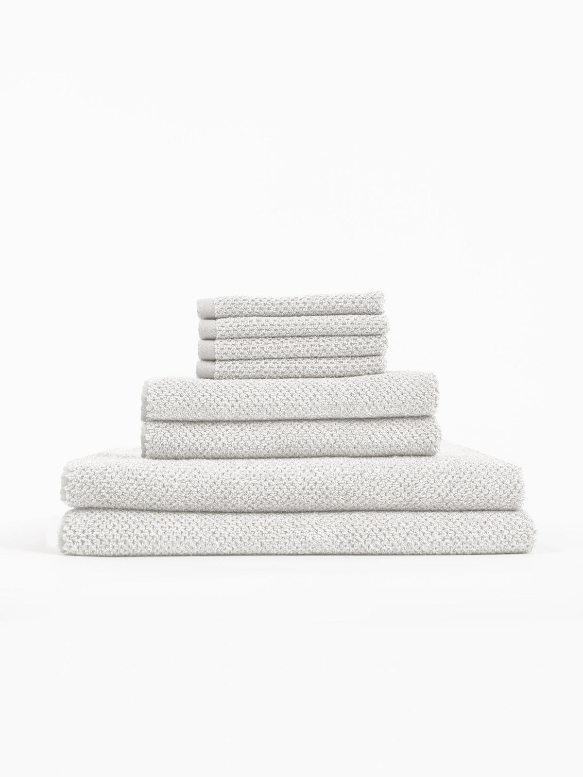 The Cozy Earth Nantucket Bath Towel Set features textured, light gray towels in assorted sizes, neatly stacked on a white background.|Color:Heathered Light Grey