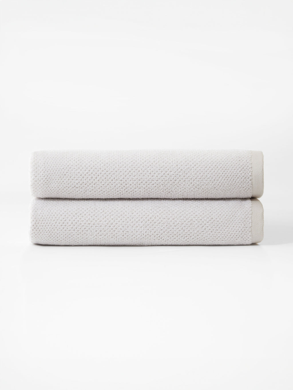 Cozy Earth’s Nantucket Bath Towel Set features two neatly folded, light gray towels stacked together against a plain white background.|Color:Heathered Light Grey