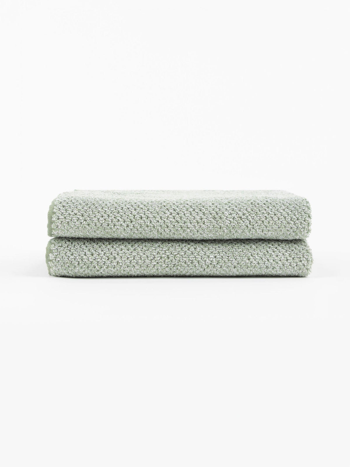 Two Nantucket Bath Towels by Cozy Earth, in a light green textured finish, are neatly folded and stacked on a white surface with a plain white background.|Color:Heathered Sage
