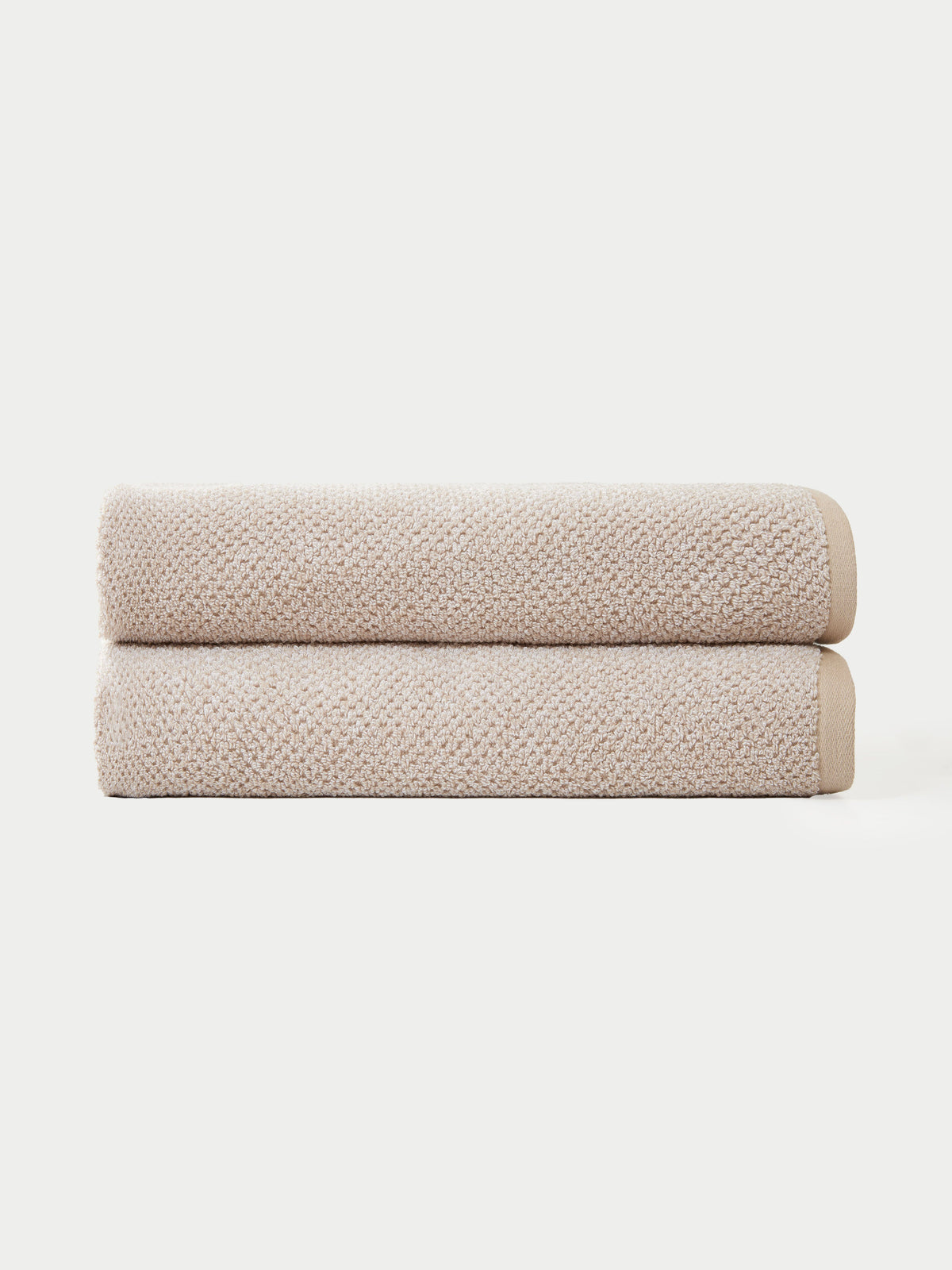 Two Nantucket Bath Towels by Cozy Earth are neatly folded and stacked together against a plain white background.|Color:Heathered Sand