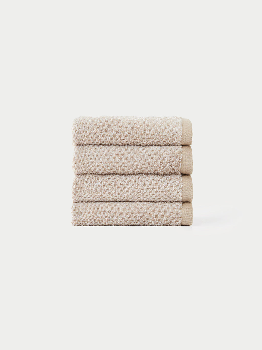 A neatly stacked pile of four beige, textured hand towels from the Cozy Earth Nantucket Bath Towel Set is displayed against a plain white background.|Color:Heathered Sand