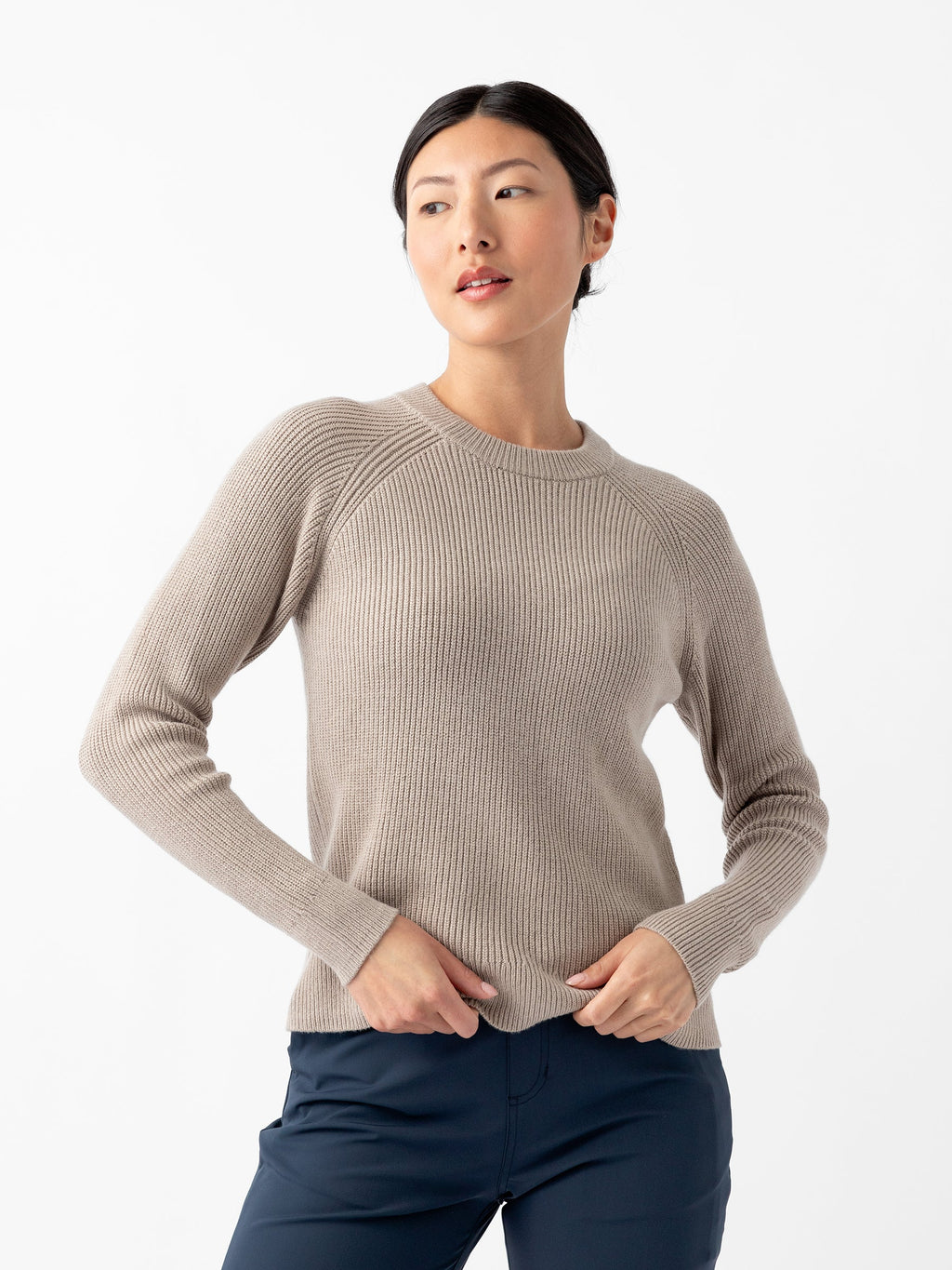 A person stands against a plain white background, wearing Cozy Earth's Women's Classic Crewneck in beige and dark blue pants. The individual has dark hair tied back and is looking to the side with hands resting on the hips. |Color:Taupe