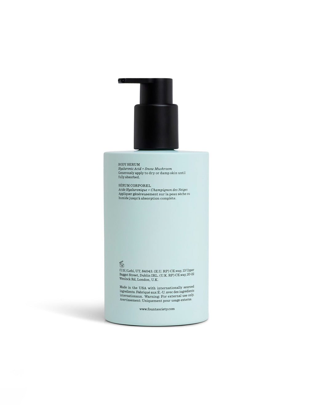 A light blue Body Serum bottle by Cozy Earth with a black pump and product info in black text on the back stands upright against a white background.