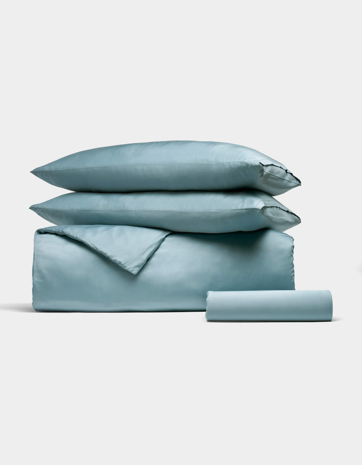 The Cozy Earth Bamboo Bedding Essential Bundle, featuring a neatly folded light blue set with two pillows, a duvet, and a rolled sheet, is stacked together on a simple light background.|Color:River