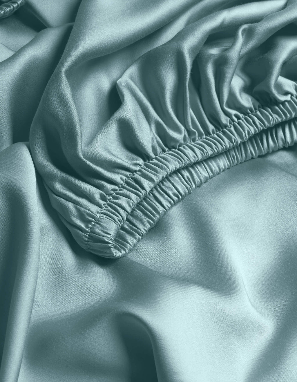 Close-up of Cozy Earth's Bamboo Fitted Sheet in light blue, featuring gathered elastic edges and a smooth, shiny texture with soft folds.|Color:River