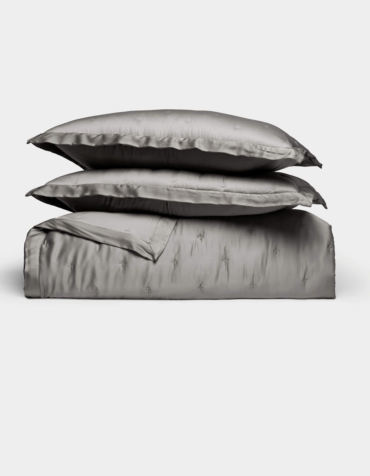 The Bamboo Quilt Bundle by Cozy Earth features lustrous silver-gray bed linens, including two stacked pillows, a folded sheet, and a duvet cover, all arranged against a plain white background.|Color:Charcoal