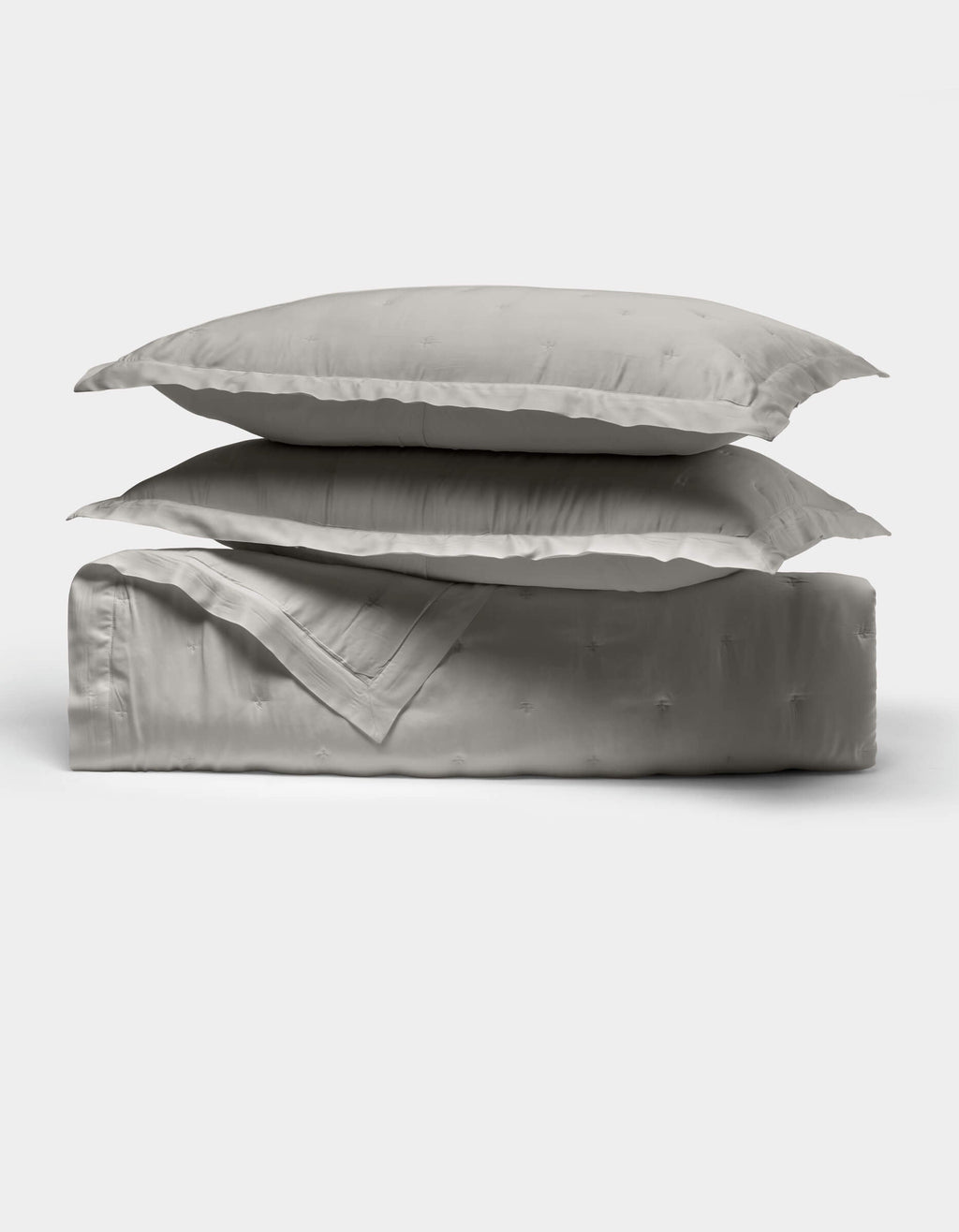 The Cozy Earth Bamboo Quilt Bundle features two light gray pillows stacked atop a folded matching comforter, all crafted from smooth, shiny fabric, displayed against a plain white background.|Color:Light Grey