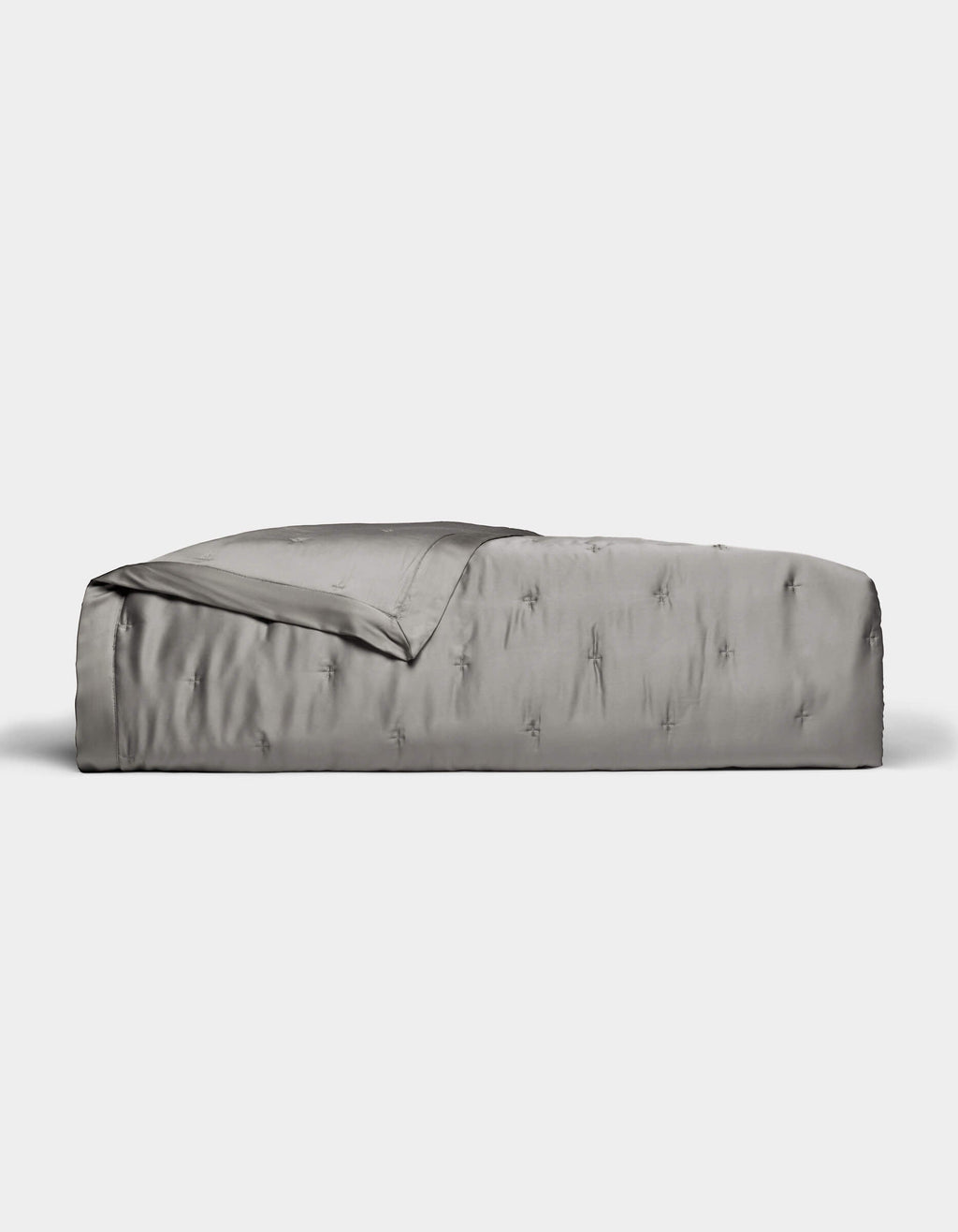 A neatly made bed features the Cozy Earth Bamboo Quilt in smooth, shiny silver-gray satin, partially folded back at the top, set against a plain white background.|Color:Charcoal