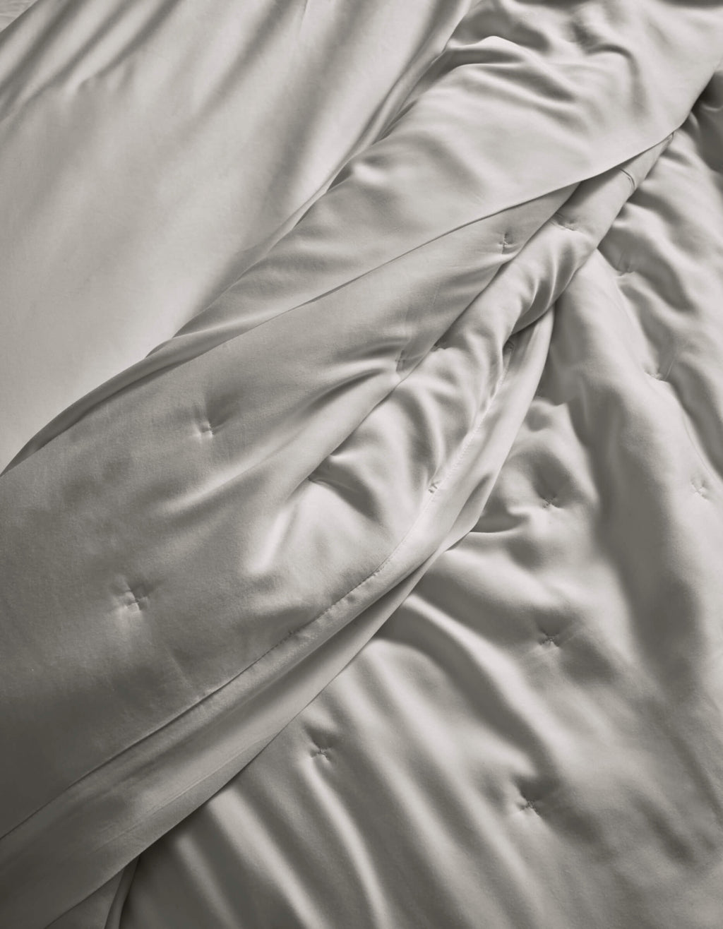 A close-up of the Cozy Earth Bamboo Quilt, in light gray, softly draped with subtle button tufting, highlights its smooth and silky fabric.|Color:Light Grey