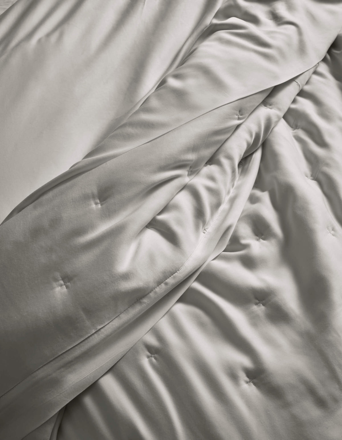 A close-up of the Cozy Earth Bamboo Quilt, in light gray, softly draped with subtle button tufting, highlights its smooth and silky fabric.|Color:Light Grey