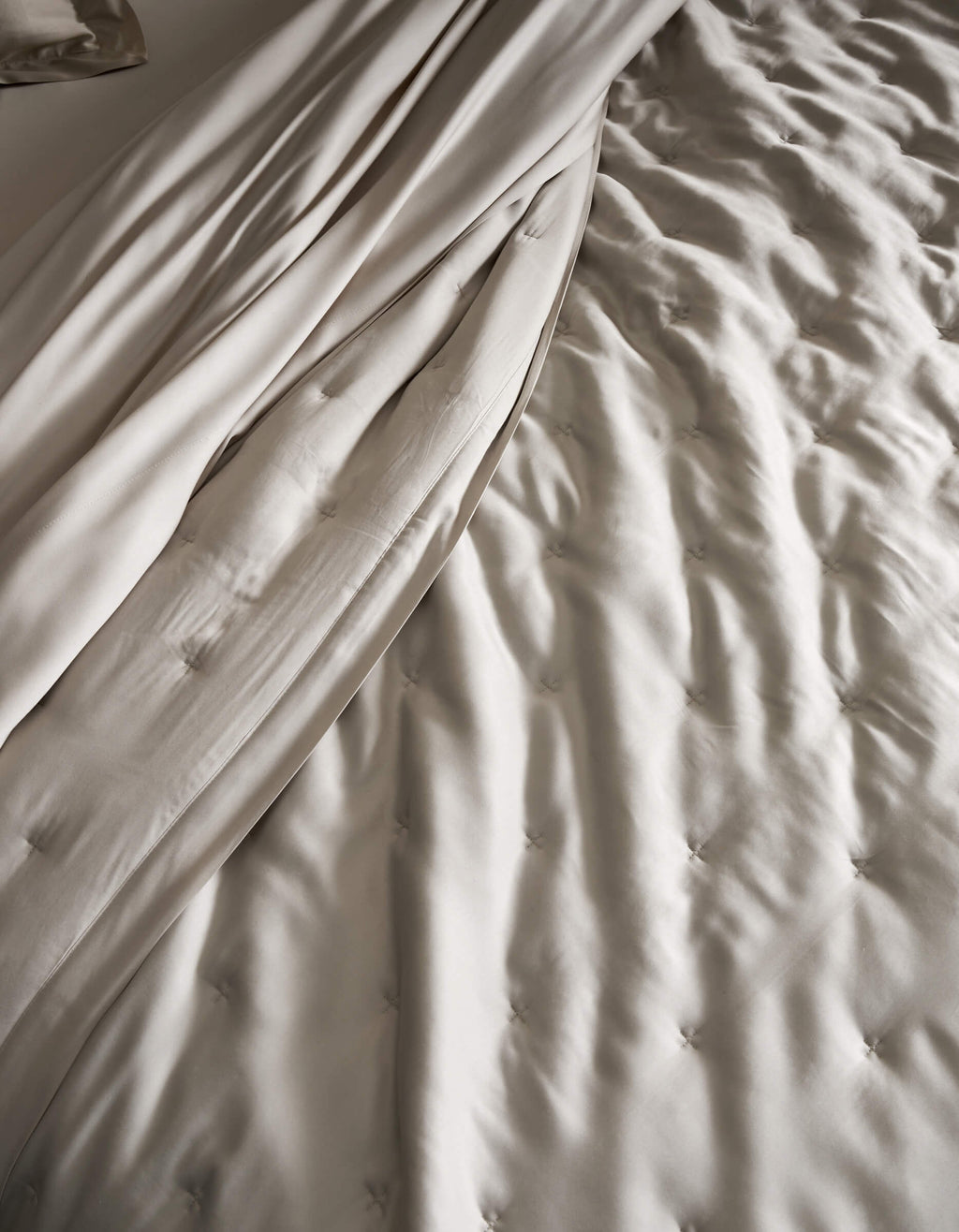 A close-up of a neatly made bed featuring the Cozy Earth Bamboo Quilt, showcasing its light beige, tufted design and smooth, draped sheets for a soft and elegant texture.|Color:Oat