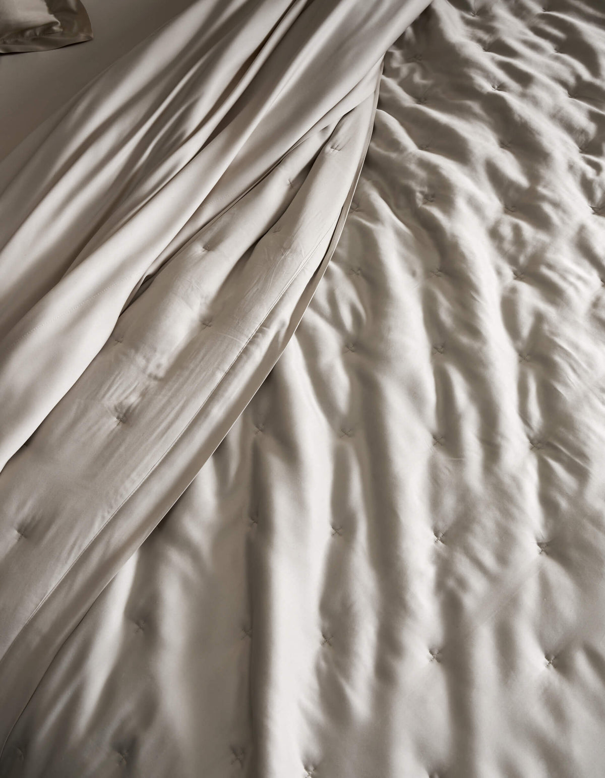 A close-up of a neatly made bed featuring the Cozy Earth Bamboo Quilt, showcasing its light beige, tufted design and smooth, draped sheets for a soft and elegant texture.|Color:Oat