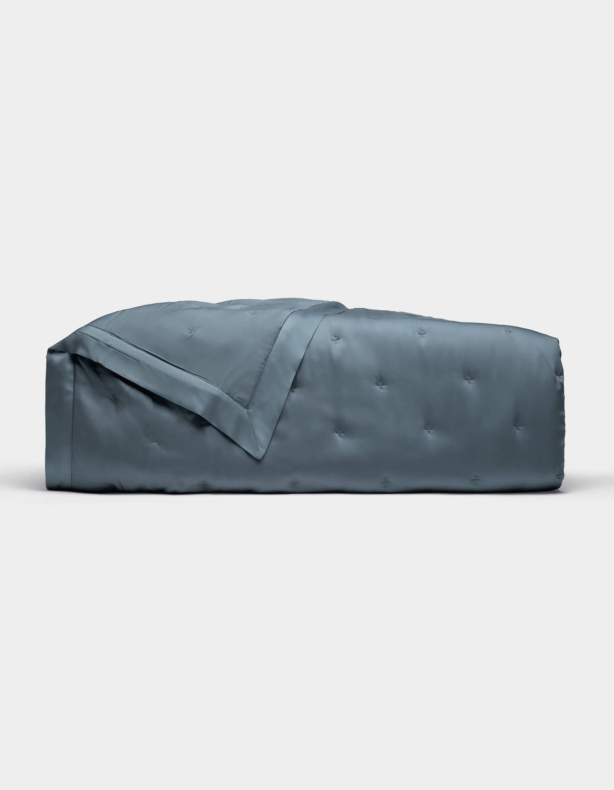 The Cozy Earth Bamboo Quilt, shown folded against a plain white background, features a blue-gray color with a subtle quilted pattern and smooth, shiny finish.|Color:Pacific Blue