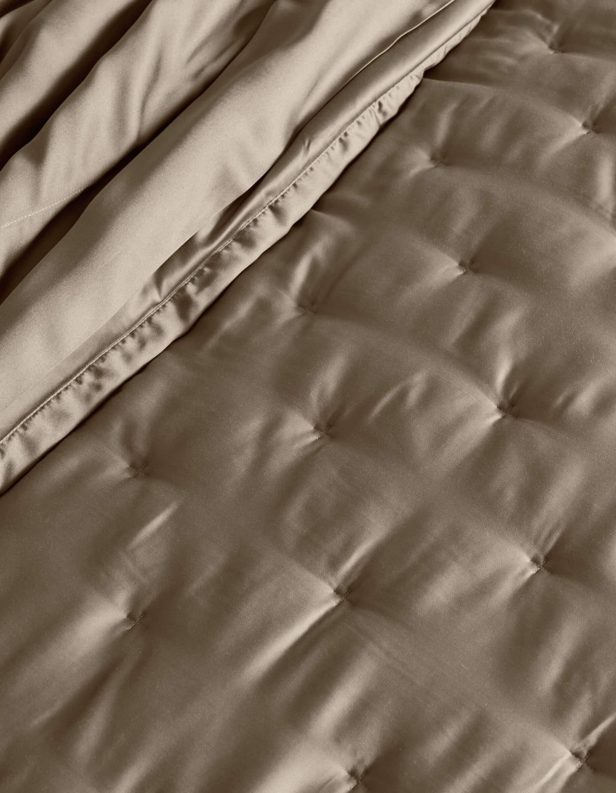 A close-up of the Cozy Earth Bamboo Quilt shows its quilted, taupe surface with stitched square patterns and a folded edge, highlighting the soft, smooth fabric texture.|Color:Walnut