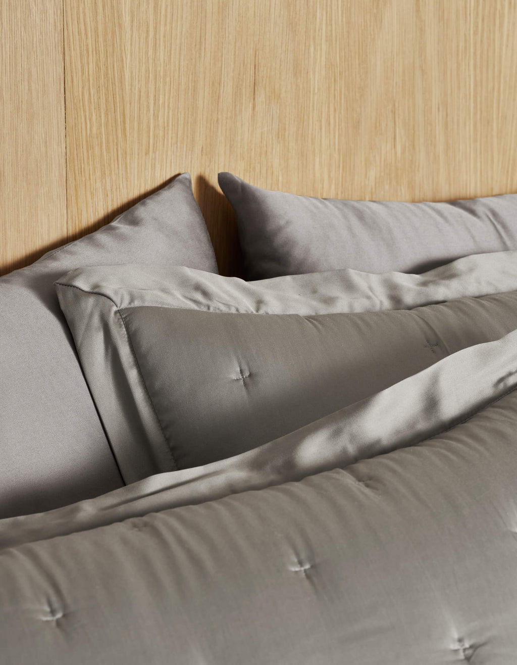 A bed featuring Cozy Earth's Bamboo Quilted Shams in light gray and a matching comforter with stitched detailing. A light wood headboard adds warmth to the neutral bedding ensemble.|Color:Charcoal