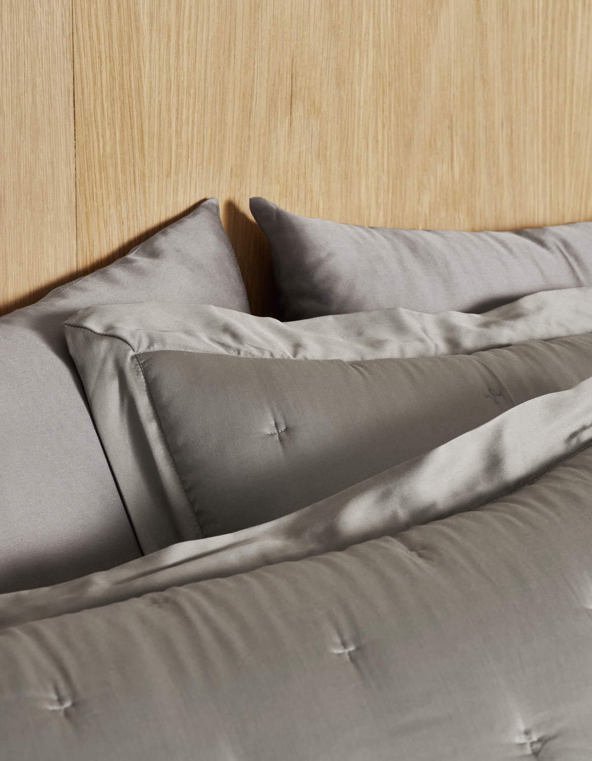 A bed featuring Cozy Earth's Bamboo Quilted Shams in light gray and a matching comforter with stitched detailing. A light wood headboard adds warmth to the neutral bedding ensemble.|Color:Charcoal