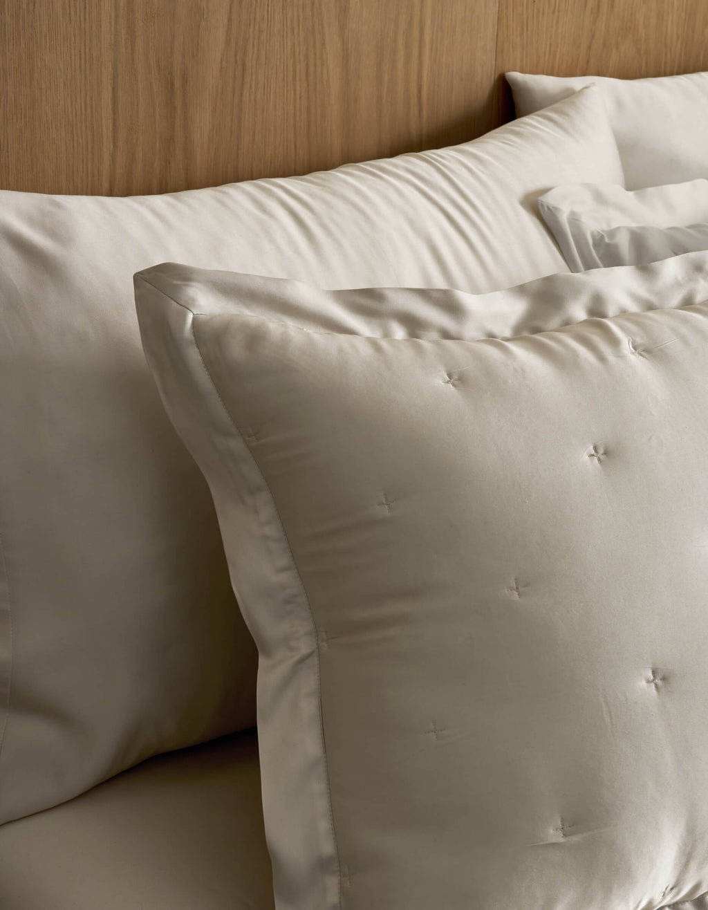 Close-up of Cozy Earth Bamboo Quilted Shams on a bed, featuring cream-colored square shams with subtle tufted details and larger rectangular pillows arranged neatly against a wooden headboard.|Color:Oat