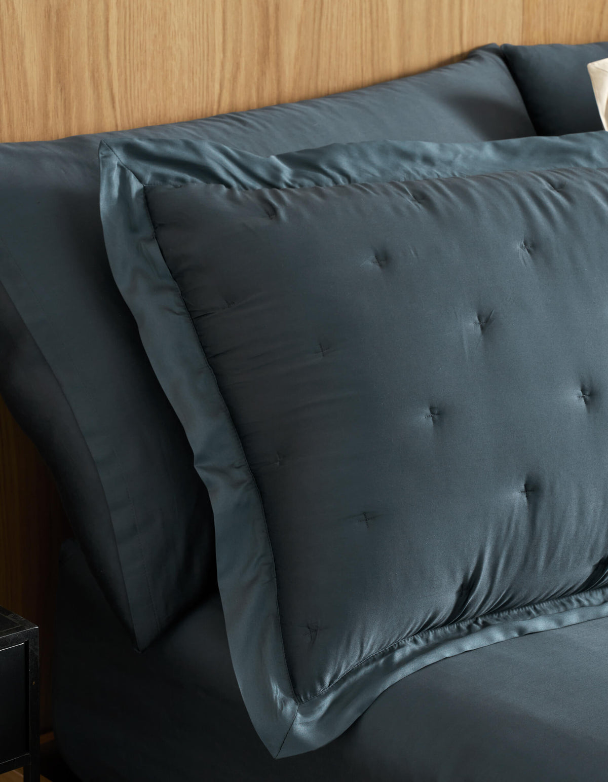 A close-up of a neatly made bed features Cozy Earth Bamboo Quilted Shams and matching sheets in dark blue, set against a light wood headboard.|Color:Pacific Blue