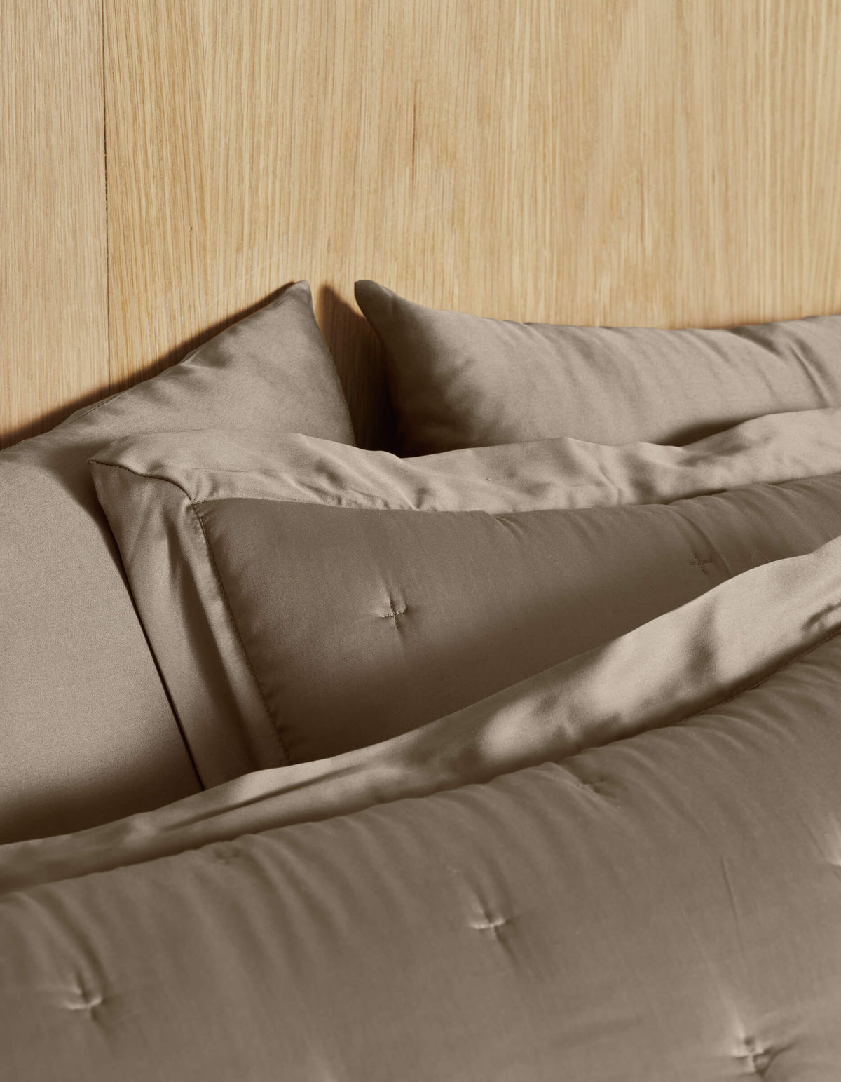 Close-up of Cozy Earth Bamboo Quilted Shams, neatly arranged in taupe on a bed with a light wood headboard, creating a calm and cozy atmosphere.|Color:Walnut