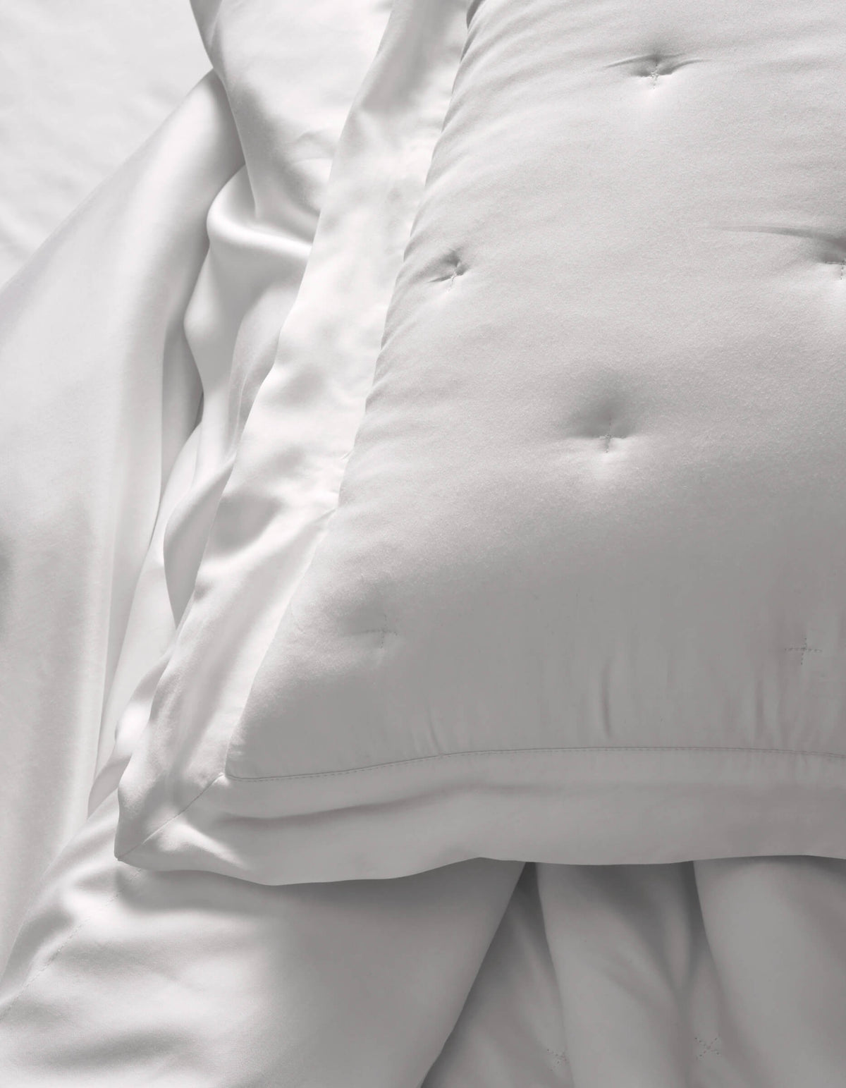 A close-up of Cozy Earth Bamboo Quilted Shams resting on smooth white sheets creates a soft, clean look. The bedding appears fluffy and inviting.|Color:White