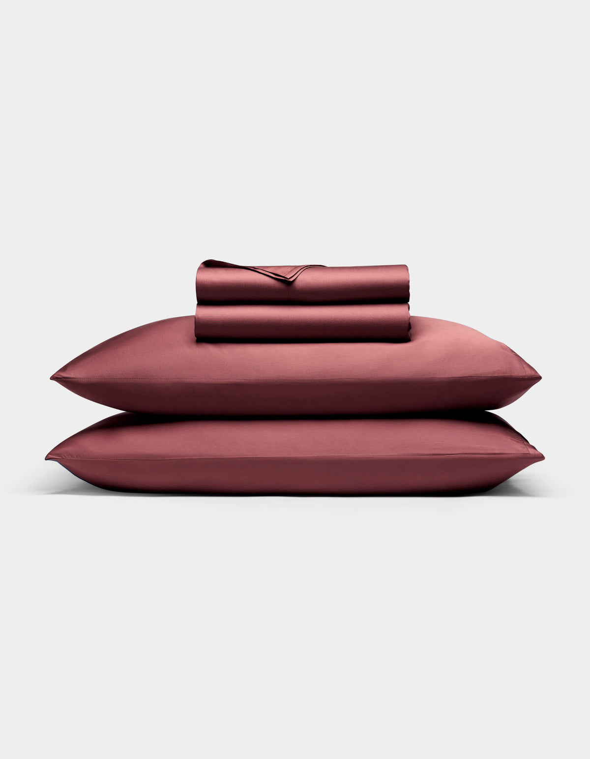 A neatly folded Bamboo Sheet Set by Cozy Earth, including bed sheets and pillowcases in deep burgundy, is stacked on two matching pillows against a plain light gray background.|Color:Mulberry