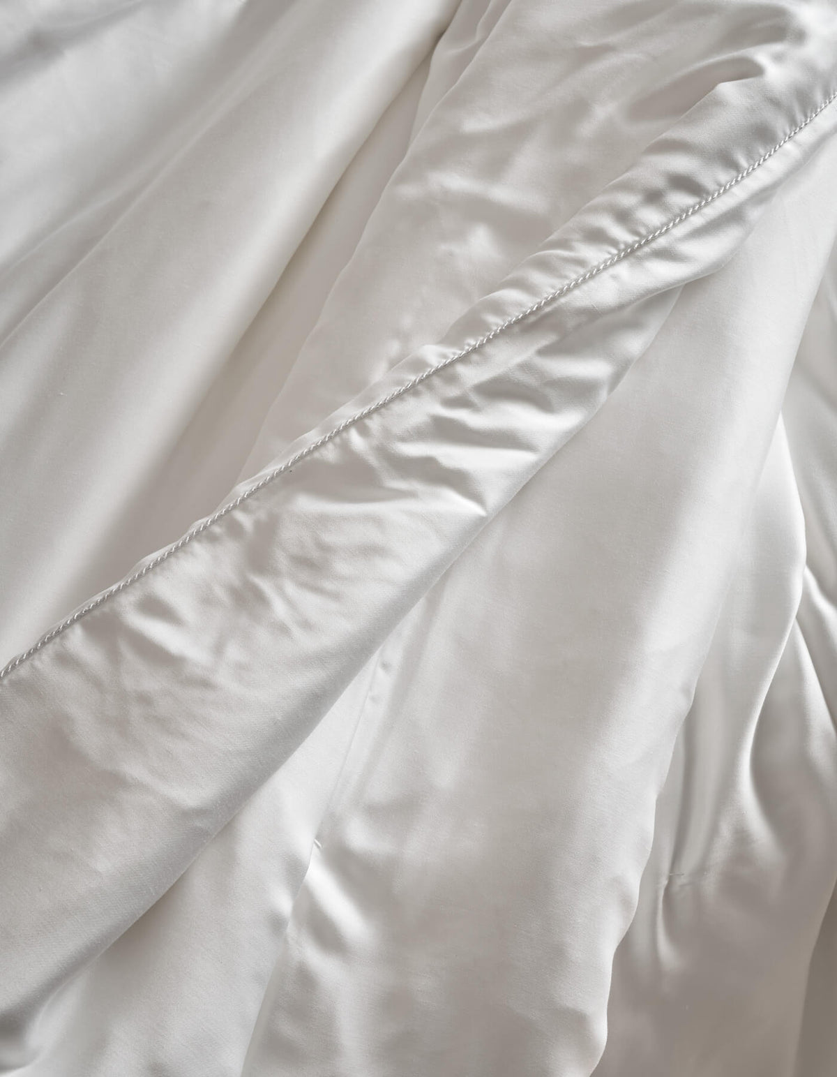 Close-up of Cozy Earth Silk Comforter: soft, white fabric with a diagonal seam, gentle folds, and smooth, shiny texture.|Filling:Extra