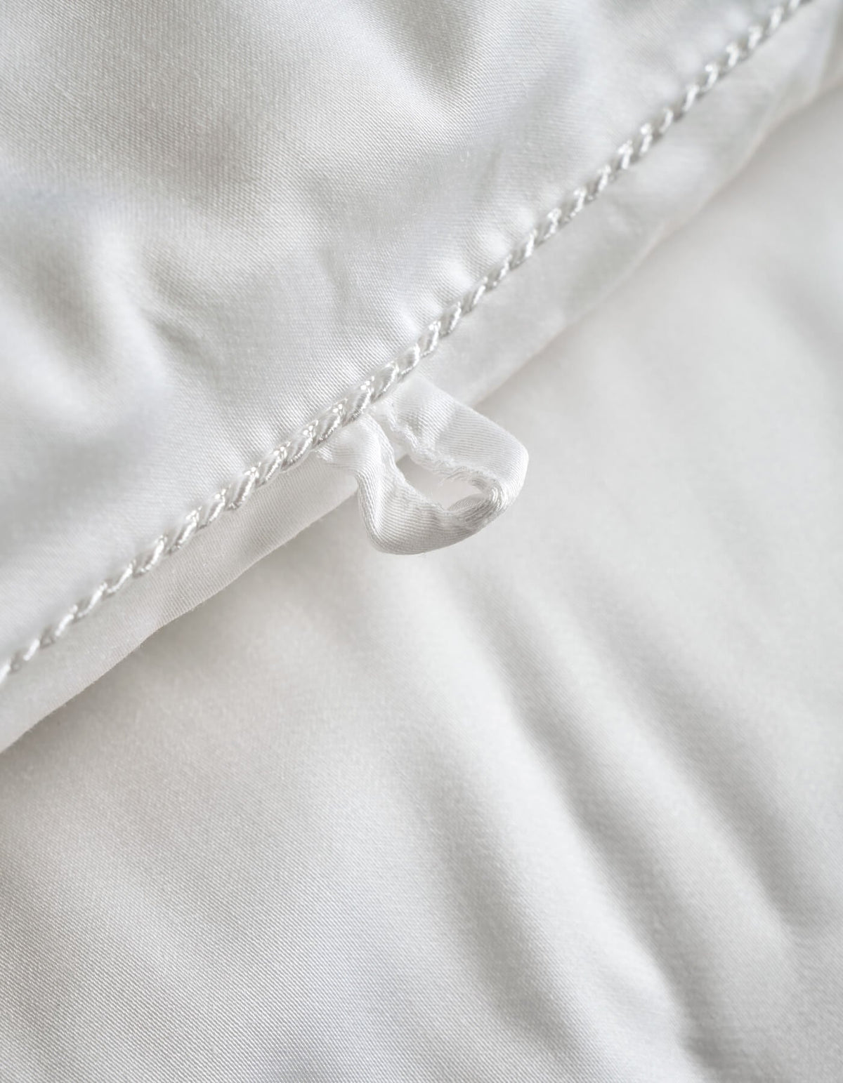 Close-up of the Cozy Earth Silk Comforter, featuring a white surface with a fabric loop sewn into the edge and detailed seam stitching. The smooth and soft texture showcases its luxurious comfort.|Filling:Extra
