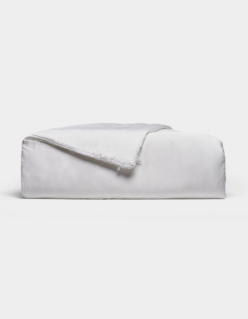 A neatly folded, fluffy Silk Comforter by Cozy Earth is placed against a plain light background. The fabric appears smooth and soft, highlighting its plush and inviting texture.|Filling:Extra