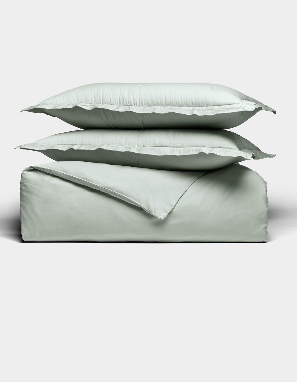 Two light gray pillows are stacked atop a matching folded Soft-Wash Cotton Duvet Set by Cozy Earth, all set against a plain white background. The bedding appears soft and smooth, highlighting its cozy and minimal aesthetic.|Color:Laurel