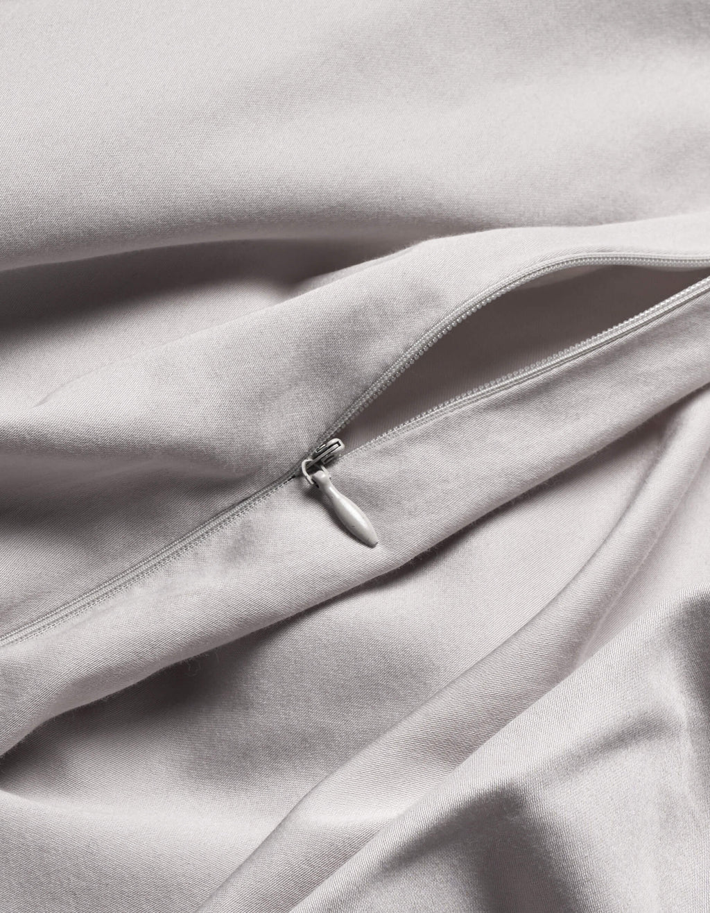 A close-up of Cozy Earth's Soft-Wash Cotton Duvet Cover in light grey shows a silver zipper partially unzipped on its smooth, gently folded fabric.|Color:Dew