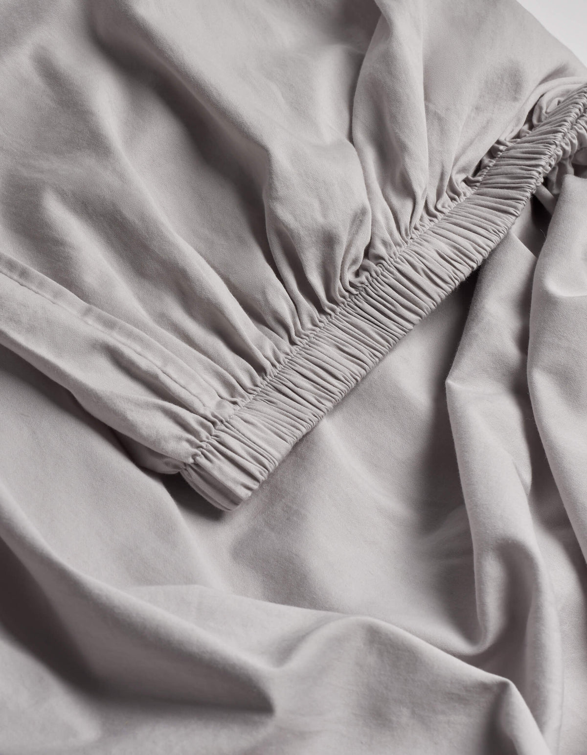 A close-up of the Cozy Earth Soft-Wash Cotton Fitted Sheet highlights its light gray color, gathered elastic edge, and ultra-soft fabric texture.|Color:Dew