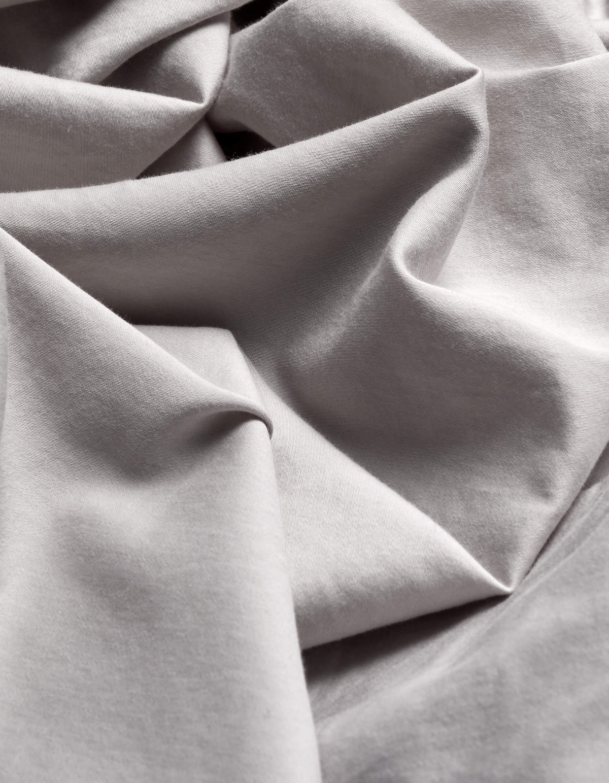 Close-up of the Cozy Earth Soft-Wash Cotton Flat Sheet in light grey, featuring flowing folds and gentle shadows that highlight its smooth texture and elegant drape.|Color:Dew
