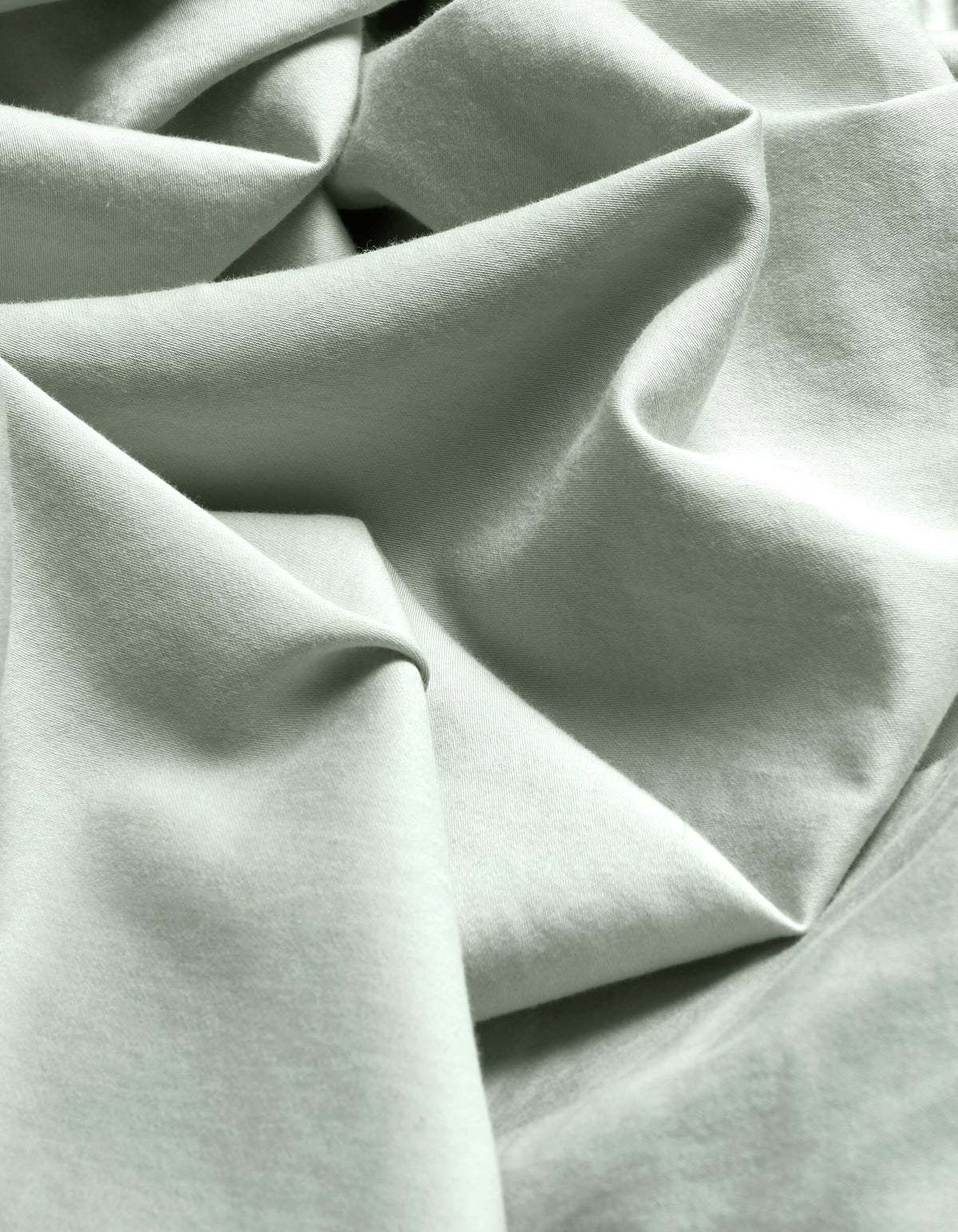 Close-up of Cozy Earth's Soft-Wash Cotton Flat Sheet in light mint green, featuring soft folds, gentle wrinkles, a subtle weave, and delicate shadows.|Color:Laurel