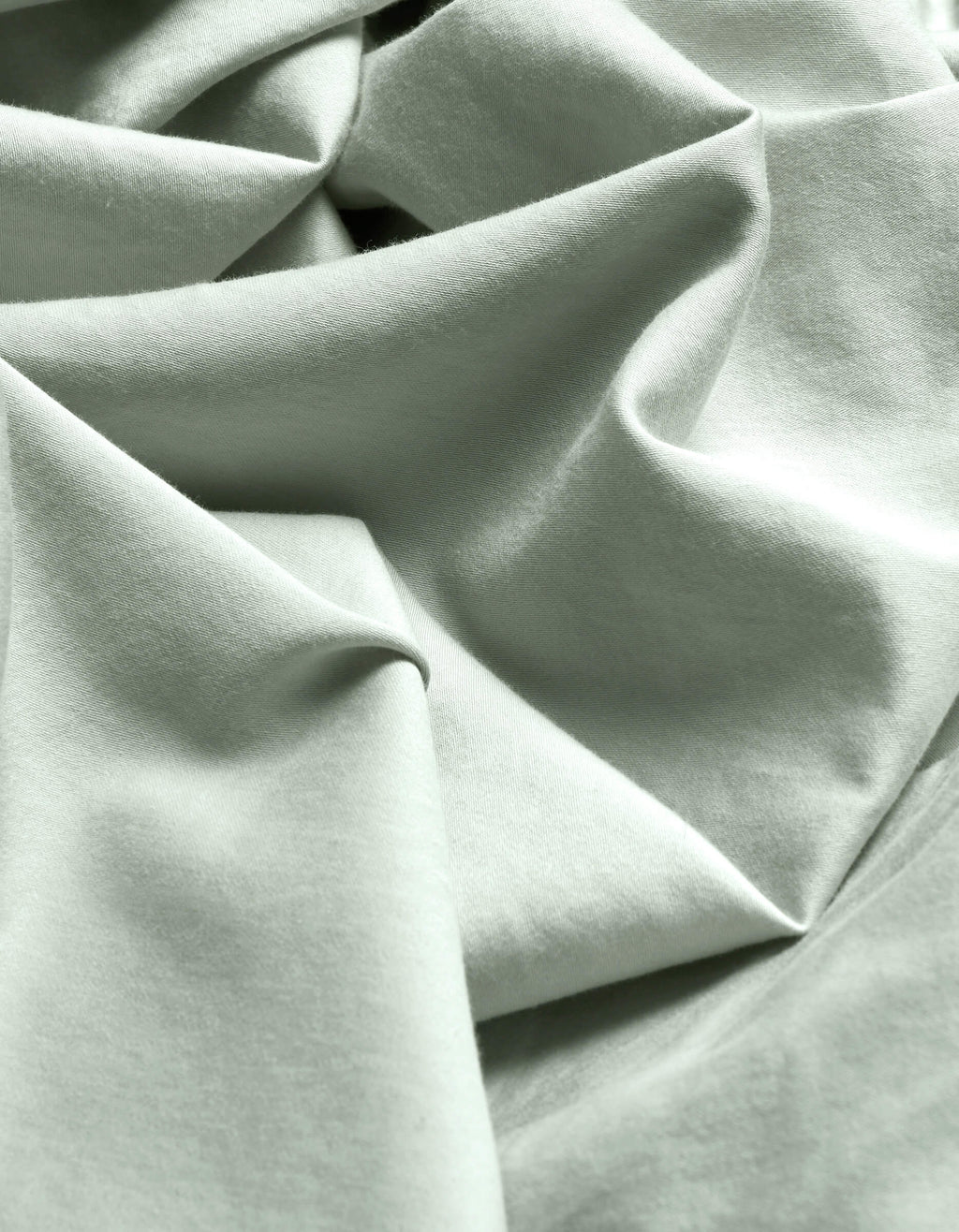 Close-up of Cozy Earth's Soft-Wash Cotton Flat Sheet in light mint green, featuring soft folds, gentle wrinkles, a subtle weave, and delicate shadows.|Color:Laurel