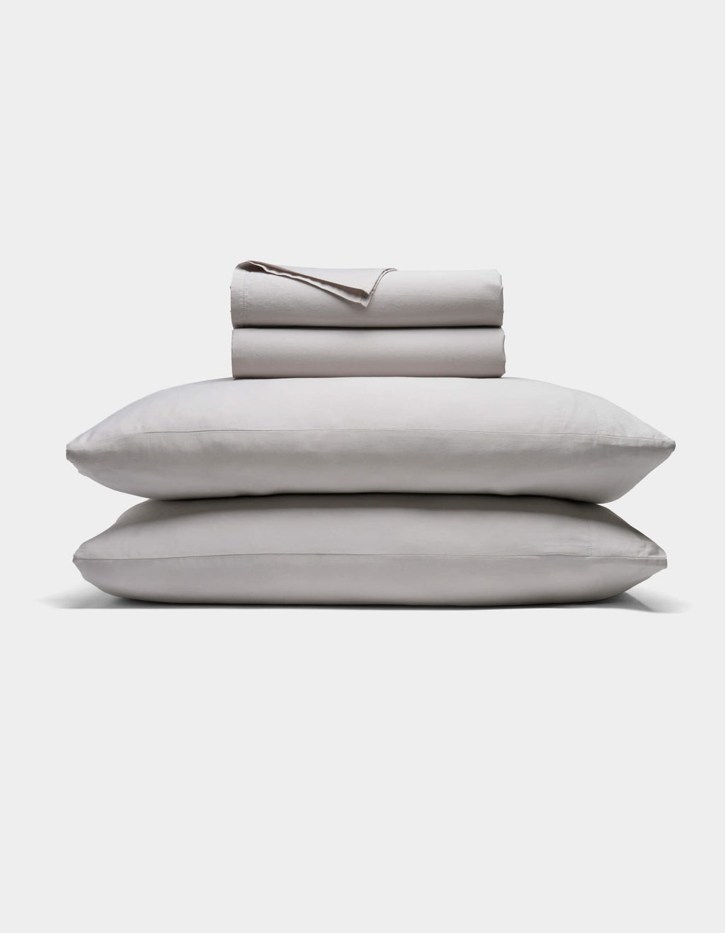 A neatly folded Soft-Wash Cotton Sheet Set by Cozy Earth in light gray is stacked atop two matching pillows, all set against a plain white background.|Color:Dew