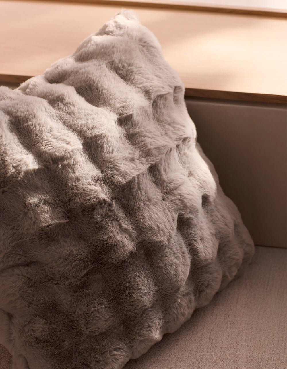 The Cozy Earth Bubble Cuddle Pillow, featuring soft, textured light grey faux fur, rests on a beige surface as natural light casts gentle shadows.|Color:Light Grey |Size:Euro
