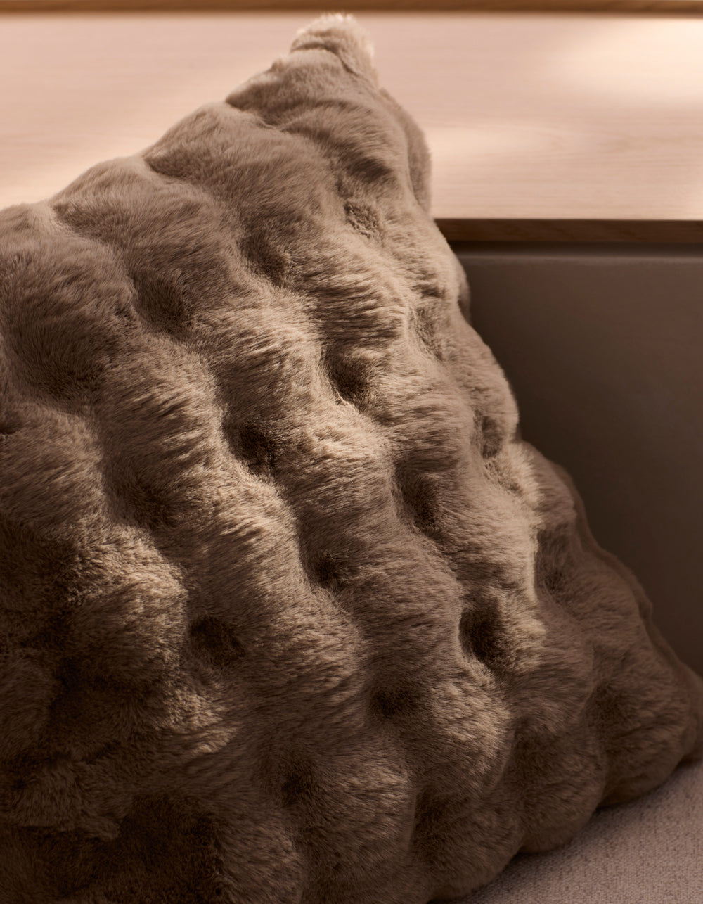 The Cozy Earth Bubble Cuddle Pillow, with its plush brown wavy tufted texture, rests on a light wooden bench in soft natural light.|Color:Walnut |Size:24" x 24"