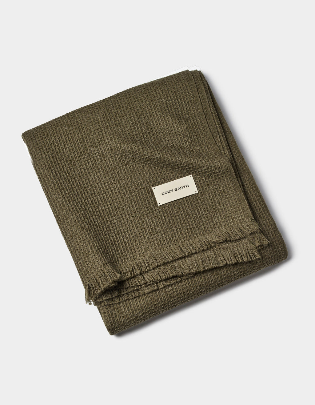 A folded olive green Alpaca Waffle Throw by Cozy Earth features a waffle texture, fringed edges, and a white tag with the brand name, set against a plain white background.|Color:Utility Green