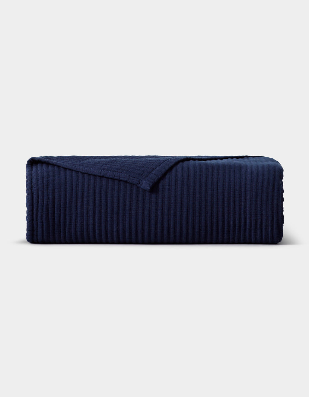 The Cozy Earth Bamboo Coverlet, in dark navy blue with a ribbed texture and one corner turned down, is displayed neatly against a plain light gray background.|Color:Navy