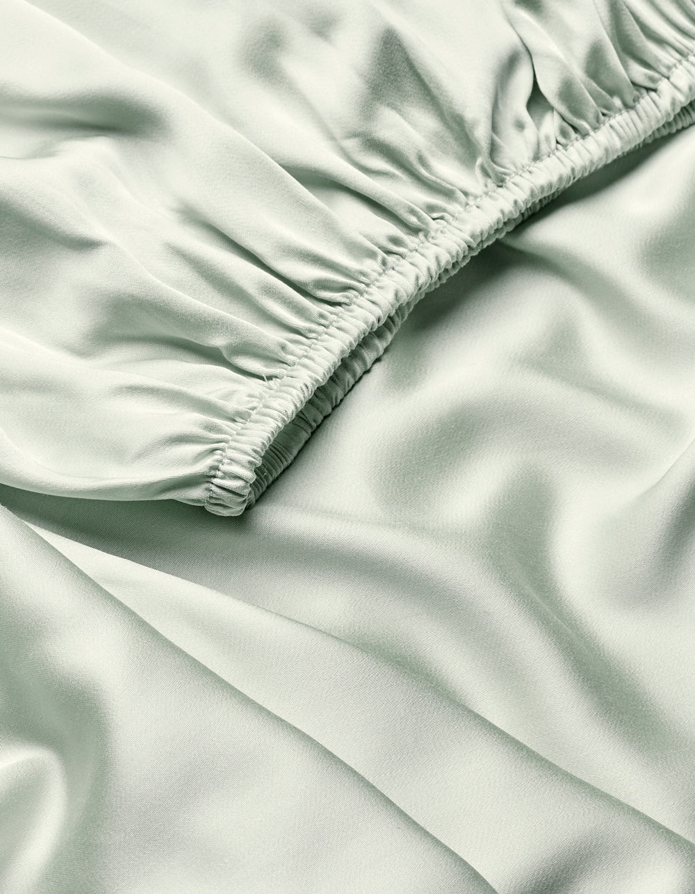 Close-up of Cozy Earth’s Bamboo Fitted Sheet in light green, showing silky fabric with a diagonal ruched seam that creates soft folds and a smooth, shiny texture.|Color:Laurel