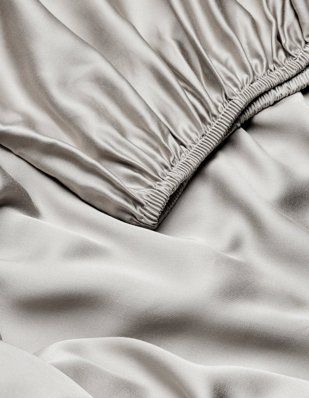 Close-up of Cozy Earth Bamboo Fitted Sheet in light gray, featuring a gathered elastic waistband and showcasing its smooth, shiny, slightly wrinkled satin texture.|Color:Light Grey
