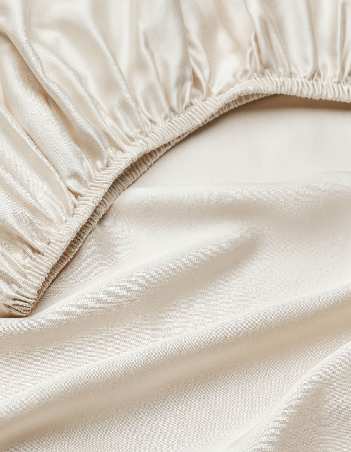 Close-up of Cozy Earth's Bamboo Fitted Sheet in smooth, ivory-colored satin with an elastic edge, highlighting its shiny, soft texture.|Color:Oat