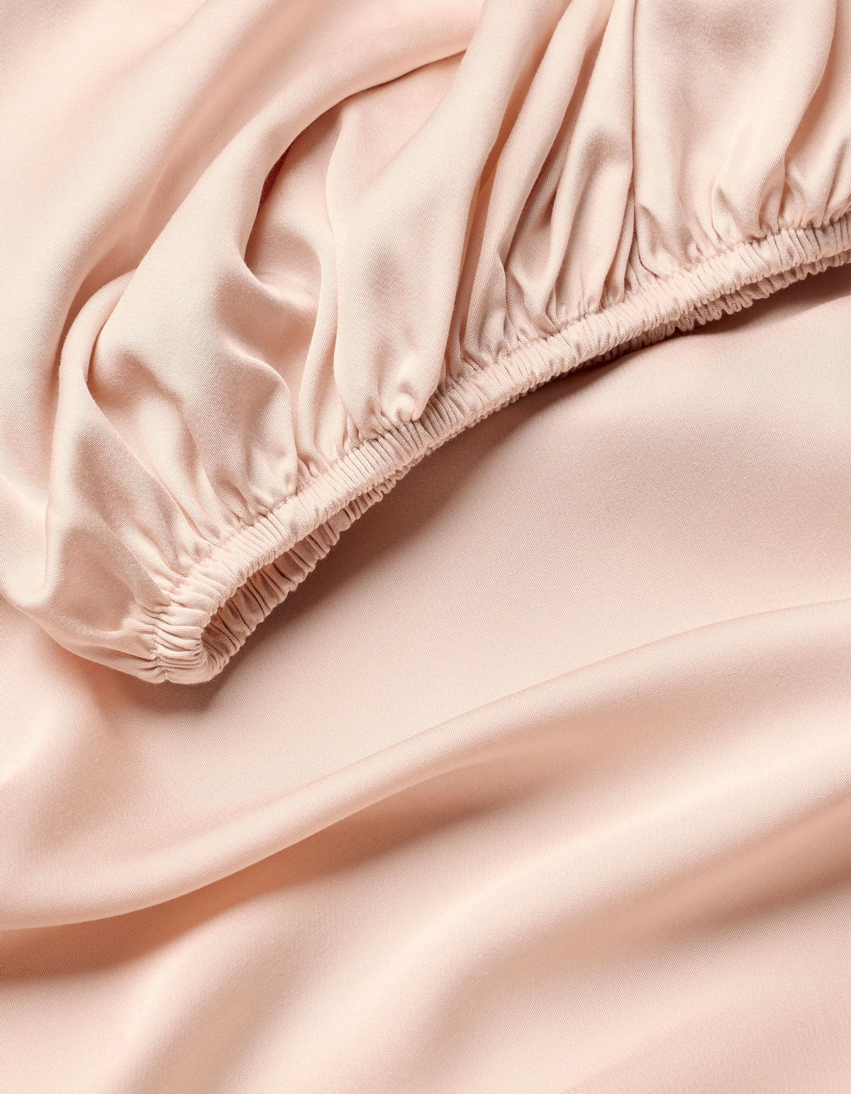Close-up of Cozy Earth Bamboo Fitted Sheet in pale pink, featuring soft, flowing folds and gathered elastic detail for a smooth, shiny texture.|Color:Peony