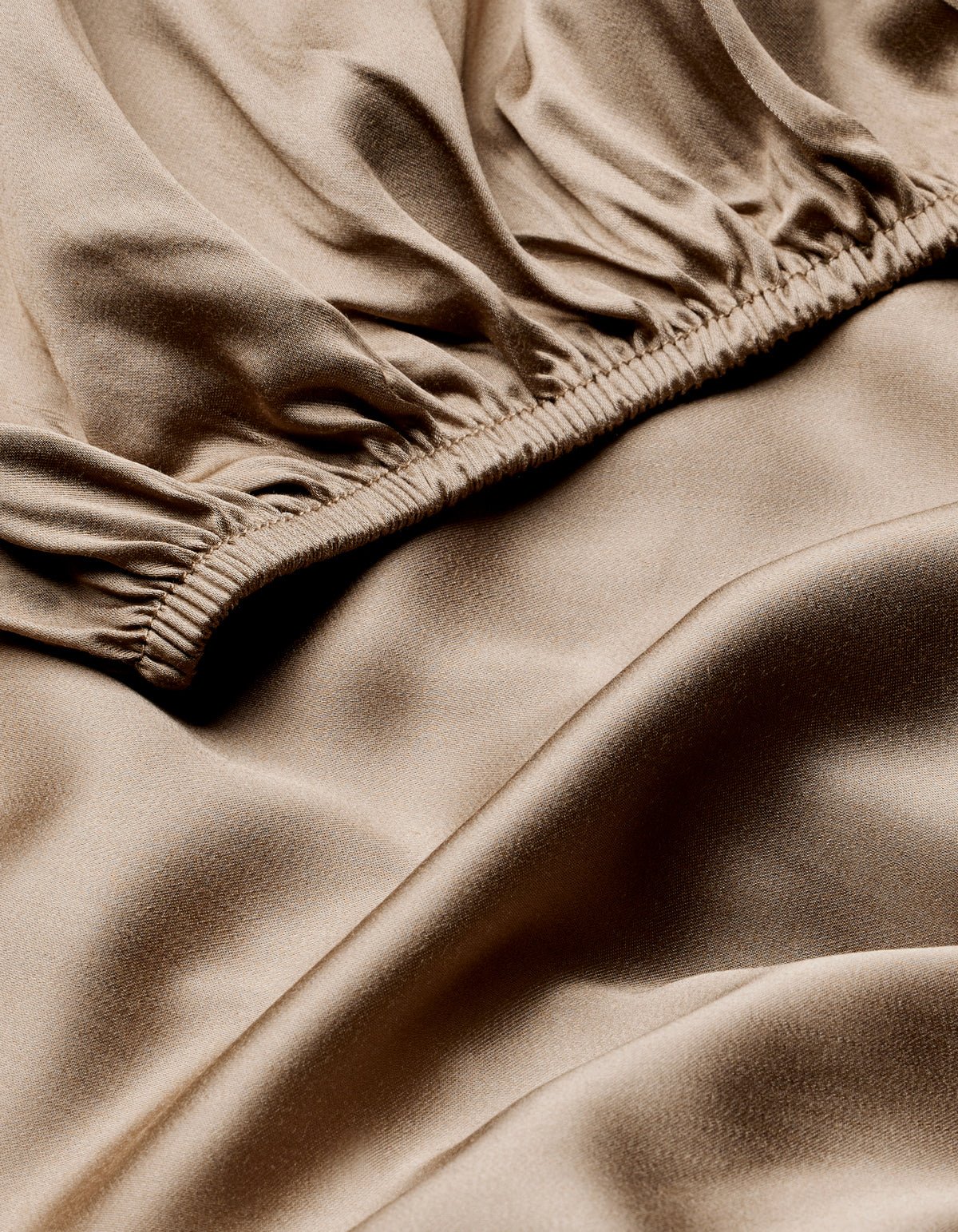 Close-up of Cozy Earth's Bamboo Fitted Sheet showcases its smooth, shiny beige fabric with gathered, ruched details and gentle folds for a soft, flowing texture.|Color:Walnut